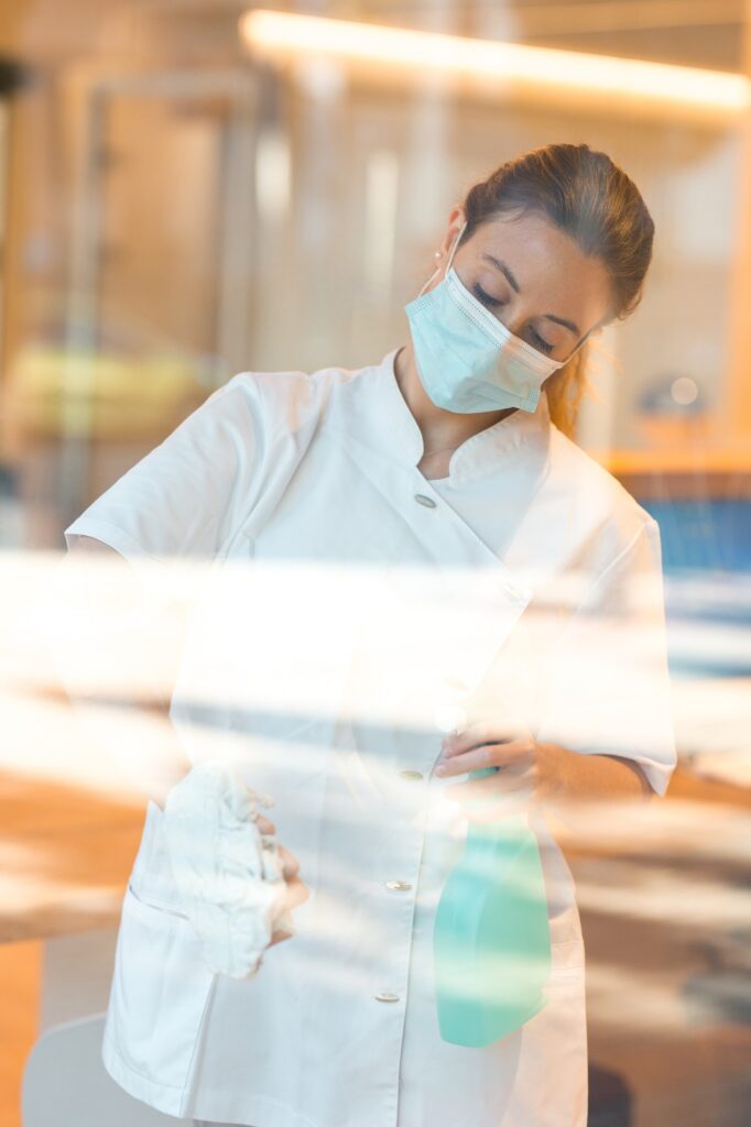 Cleaning lady using a face mask while cleaning the window of a spa or health center.